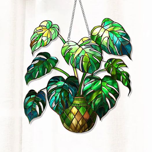 A vibrant stained glass Monstera plant, capturing the lush green hues of its leaves, hangs elegantly, reflecting light beautifully.