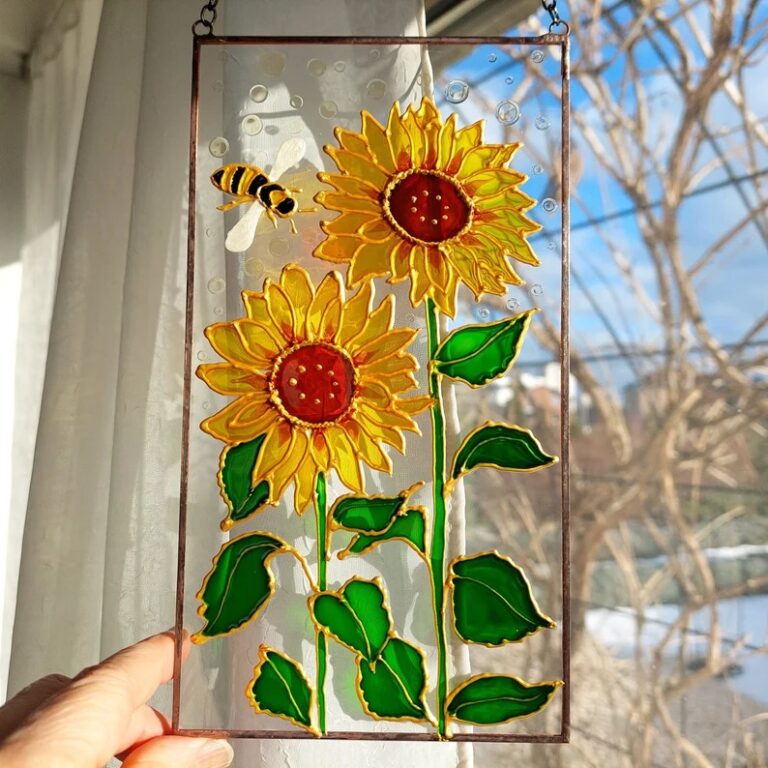 A charming stained glass piece featuring two bright sunflowers with vibrant green leaves, accompanied by a buzzing bee, capturing a cheerful scene in the sunlight.